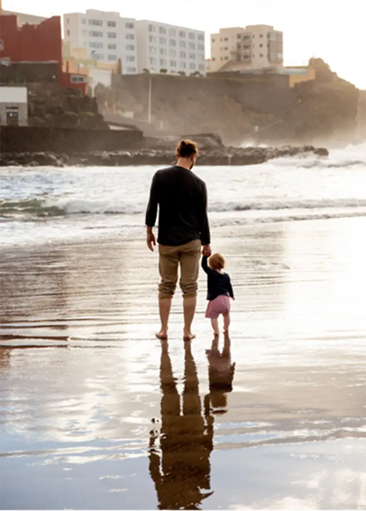 A man walking on the shore holding a child's hand